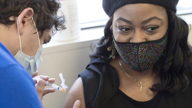 Tamika华盛顿, 谁戴着珠宝面具, 十字架项链和贝雷帽, 当医护人员准备插入装满COVID-19疫苗的注射器时，她把目光从裸露的手臂上移开.